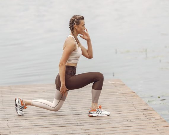 A woman performs lunges on a lakeside wooden deck, showcasing a fit lifestyle outdoors.